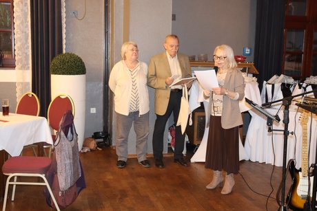 Drei Personen stehen vorne und eine Frau spricht zu den Anwesenden.