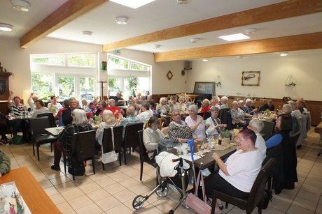 Mehrere Menschen sitzen anlangen Tischen.