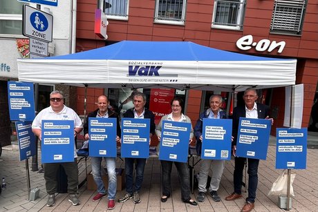 Menschen stehen vor dem VdK-Stand und halten Plakate mit Forderungen zur Kommunalwahl in die Höhe.