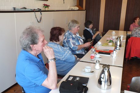 Vier Personen sitzen an einem langen Tisch und h&ouml;ren dem Referenten zu.