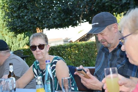 Ein Mann tippt auf seinem Handy, rechts und links von ihm sitzen zwei Frauen mit Getränken in der Hand