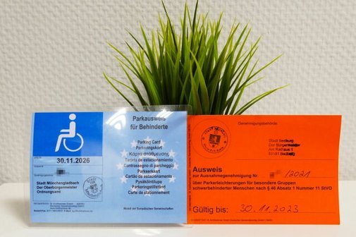 Ein klassischer blauer Behindertenausweis neben einem orangen Parkausweis f&uuml;r Sonderparkgenehmigungen.
