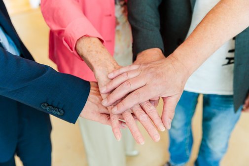 Vier Arme reichen ins Bild, die H&auml;nde in der Bildmitte &uuml;bereinandergelegt.