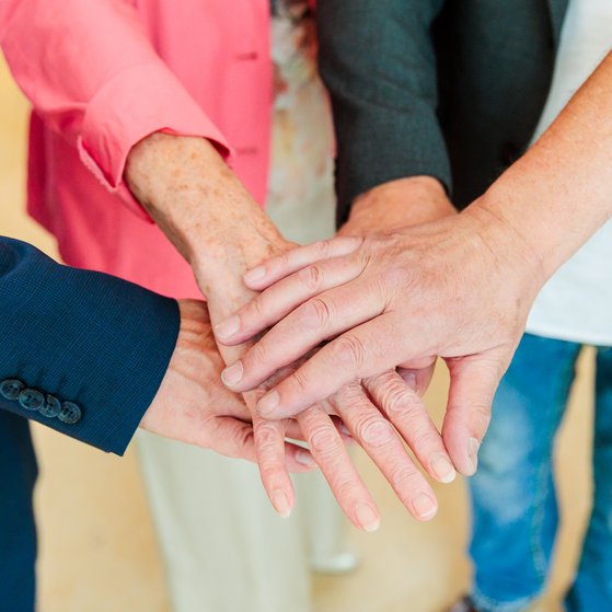 Vier Arme reichen ins Bild, die H&auml;nde in der Bildmitte &uuml;bereinandergelegt.