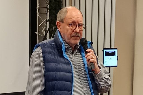 Vorstandsvorsitzender Arno Wachtel Auf dem Bild sieht man den Vorsitzenden des VdK OV Bilk, Man sieht einen älteren Herren mit Brille und blauer Weste mit einem Mikrofon in der Hand.