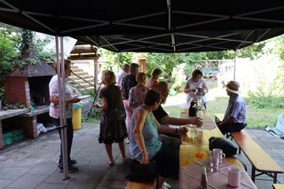 Mitglieder stehen draußen vor dem Grill an und andere sitzen am Tisch.