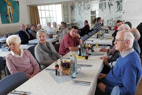 Viele Menschen sitzen in einem Saal an langen Tischen.