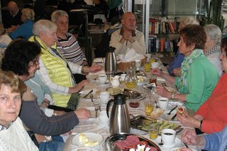 Viele Menschen sitzen gemeinsam beim Frühstück an einem langen Tisch.