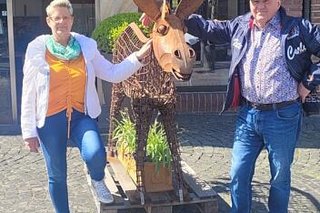 Ein Mann und eine Frau posieren neben einer Eselsskulptur aus rostrotem Cortenstahl.