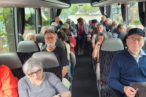 Die Mitglieder sitzen im Bus. Vorne rechts ein Rollstuhlfahrer in seinem Rollstuhl, gesichert im Bus..
