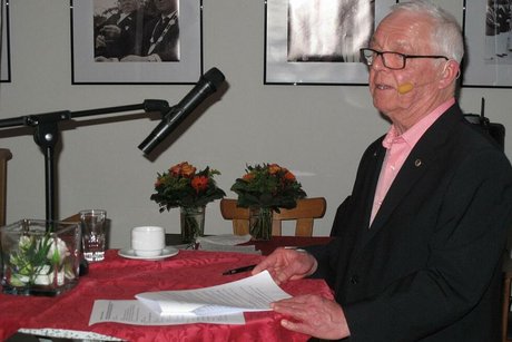 Ein Mann steht an einem Stehtisch mit Mikrofon und hält eine Rede.