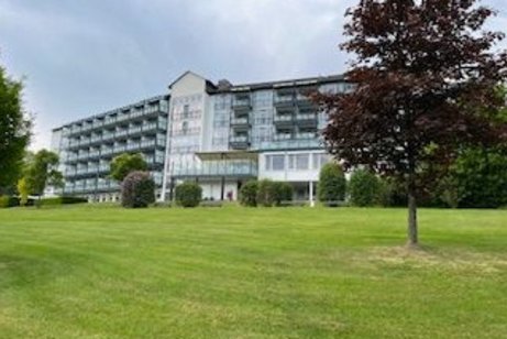 Weißes Hotelgebäude mit Wiese und Baum in Vordergrund