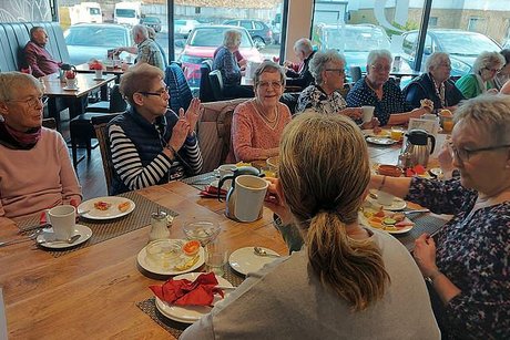 Viele Menschen sitzen gemeinsam bei einem geselligen Frühstück an einem langen Tisch.