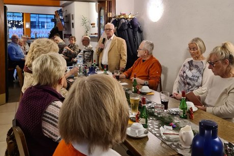 Menschen sitzen an festlich gedeckten Tischen und ein Mann h&auml;lt eine Rede.