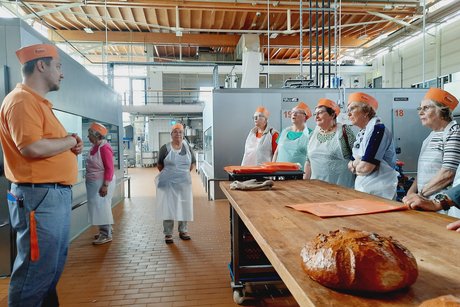 Besuch bei Bäckerei Peter. Ein Mann steht vor einer Gruppe und erklärt etwas zur Backstube.