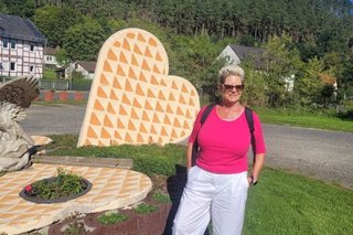 Inge Pulz, erste Vertreterin der Frauen, posiert vor einer großen Skulptur in Form von großen Waffelherzen.