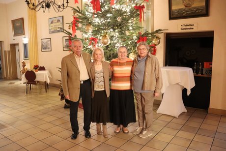 Vier Personen stehen vor einem gro&szlig;en geschm&uuml;ckten Tannenbaum.