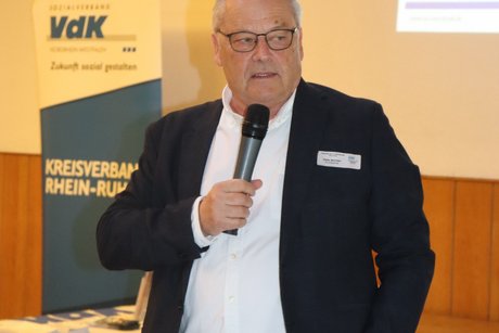 Ein Mann steht und spricht in ein Mikrophone zu den Anwesenden.