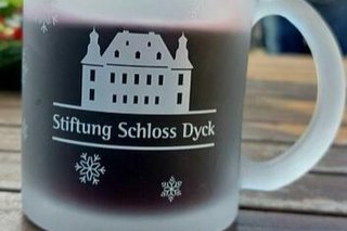 Glühwein dampft in einer Glastasse mit Gravur des Schlosses und der Inschrift Stiftung Schloss Dyck.