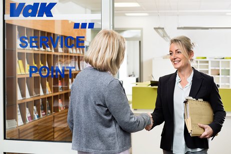 Zwei Frauen begrüßen sich vor einer Tür mit der Aufschrift VdK.