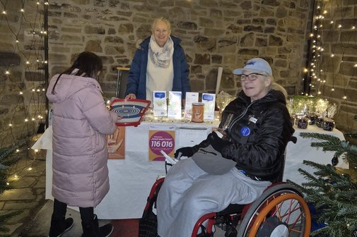 VdK Kreisverband zur Orange Week auf dem Adventsmarkt Informationsstand des VdK Kreisverbandes Mülheim an der Ruhr auf dem Adventsmarkt 2025 in der Mülheimer Altstadt. Man sieht wie die Frauenbeauftragte Christel Braun und die stellvertretende Vorsitzende Ursula Busch Informationsmaterial anbieten und ein Kind am angebotenen Tischspiel versucht einen Preis zu gewinnen.