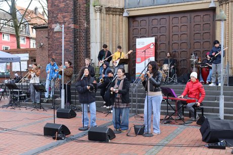 Auftaktveranstaltung internationale Wochen gegen Rassismus in Essen Holsterhausen. Jugendliche stehen auf den Kirchenstufen mit Musikinstrumenten oder vor Mikrophonen und singen.