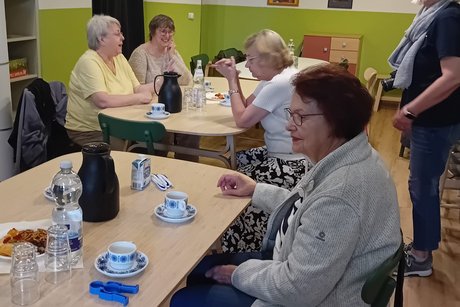 Mitglieder und Gäste des Ortsverband. Mehrere Personen sitzen an Tischen und unterhalten sich, eine Frau steht rechts und schaut die anderen an.