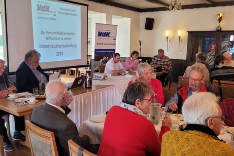 Bild aus unserer Jahreshauptversammlung aus dem Jahr 2025. Der Vorstand sitzt links am Tisch. Auf der Leinwand ist die Information zur Jahreshauptversammlung.