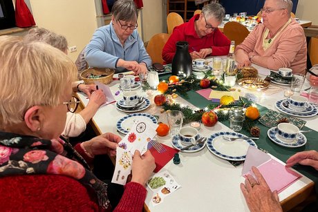 Mehrere Personen sitzen an einem Tisch und basteln Weihnachtskarten.