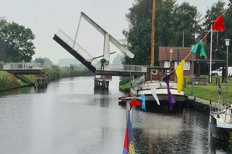 Blick vom Heck eines Schiffs auf einen Kanal und eine sich hebende Zugbrücke im Hintergrund.