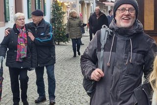 Die Besucher des Weihnachtsmarktes bummeln zwischen Buden und Häusern über das Kopfsteinpflaster. Ein Mann im Bildvordergrund rechts lacht in die Kamera.