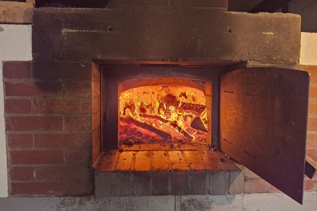 Das Bild zeigt den Backofen mit ge&ouml;ffneter Ofenklappe und voll mit brennendem Holz.