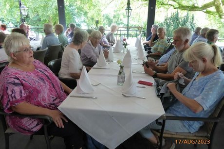 Menschen sitzen gemeinsam an einem langen, weiß eingedeckten Tisch.