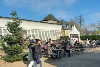 Im Innenhof des Schlosses sitzen Menschen an Bierzelttischen. Links von ihnen ist ein Tannenbaum aufgestellt. Noch scheint die Sonne vom strahlendblauen Himmel.