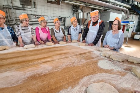 Besuch bei Bäckerei Peter. Mehrere Personen stehen an einem Tisch, auf dem Teig zum kneten liegt.