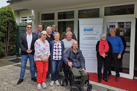 Eine kleinere Gruppe Menschen steht vor dem Eingang zu einem Lokal rechts und links von einem Roll-Up mit VdK-Logo.