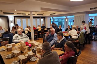 Mitglieder sitzen am Tisch und trinken Kaffee und essen ein Stück Kuchen.