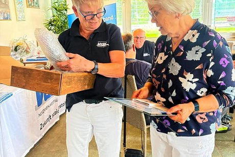 Jubilars- und Ehrenamts-Verleihung des VdK-Ortsverbandes Essen - Katernberg - Stoppenberg - Schonnebeck. Eine Frau übergibt an eine andere Frau eine Urkunde, Ehrennadel und ein Präsent.
