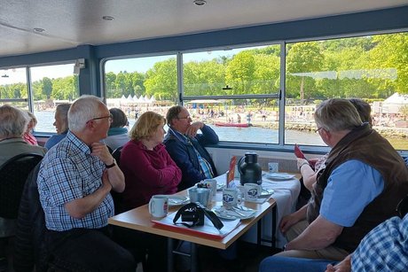 Menschen sitzen bei Getränken und Kuchen an Tischen des Ausflugschiffes.