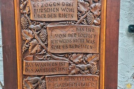 Abfotografierte Kupferplatte mit der Inschrift zu den vier Liedern, die die benachbarte Glocke zur vollen Stunde spielt: Es zogen drei Burschen wohl über den Rhein, das Lied der Loreley, das Wandern ist des Müllers Lust und Adieu, mein kleiner Gardeoffizier.