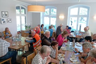 ca. 15 Personen sitzen an Tischen, essen Kuchen und trinken Kaffee