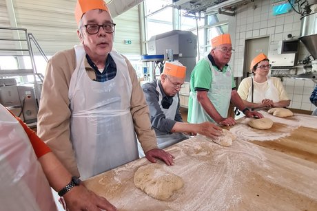 Besuch bei Bäckerei Peter. Mehrere Personen stehen an einem Tisch und kneten einen Brotteig.