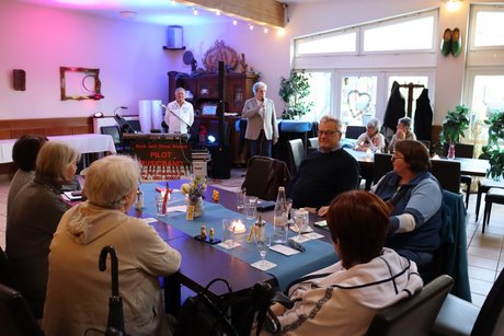 Frühlingsfest Ein Mann steht am Mikrophone im Hintergrund und spricht zu der Gruppe.