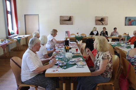 Treffen der Vertreterinnen der Frauen. Mehrere Frauen sitzen an langen Tischen und unterhalten sich miteinander.