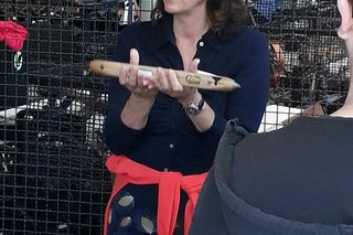 Eine Frau mit dunklen Locken und Brille hält ein altes Webschiffchen in der Hand.