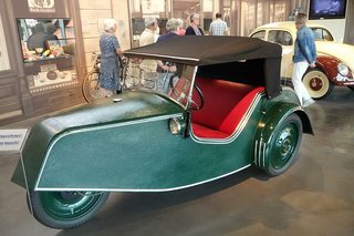 Ein dreirädriger Oldtimer, Modell Goliath Pionier, mit grüner Lackierung und roten Stoffpolstern steht in der Dr. Oetker-Ausstellung