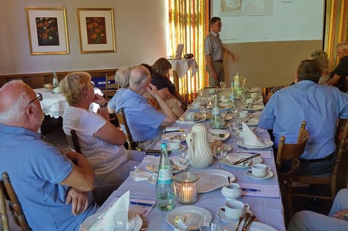 VdK-Vortragsreihe "Schutz vor Kriminalität im Alltag" Menschen sitzen an einer Kaffeetafel und blicken zum Vortragenden