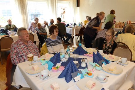 Mehrere Menschen sitzen an gedeckten Tischen und unterhalten sich miteinander.