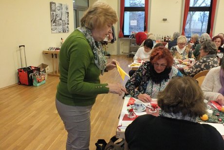 Jahresabschlusstreffen der Frauenvertreterinnen. Eine Frau steht vor einem Tisch mit anderen Frauen und schaut zu, wie sie die Blätter falten.