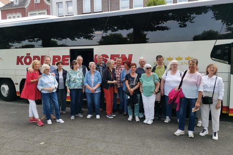 Viele Menschen stehen vor einem Reisebus zum Gruppenfoto zusammen.